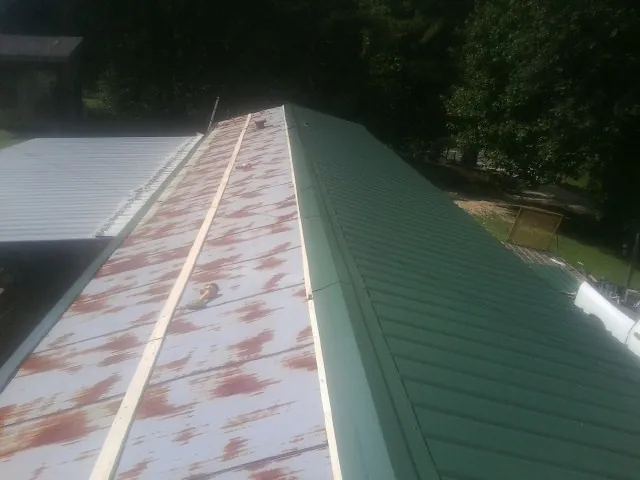 Old rusted panels beside newly installed green metal roofing — Wind Damage Roof Repair by Roofing Brothers in Hastings